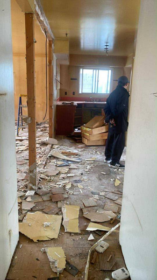 Torn-out drywall and plaster across the floor of a Calgary house being stripped back, the original kitchen cabinets still in place