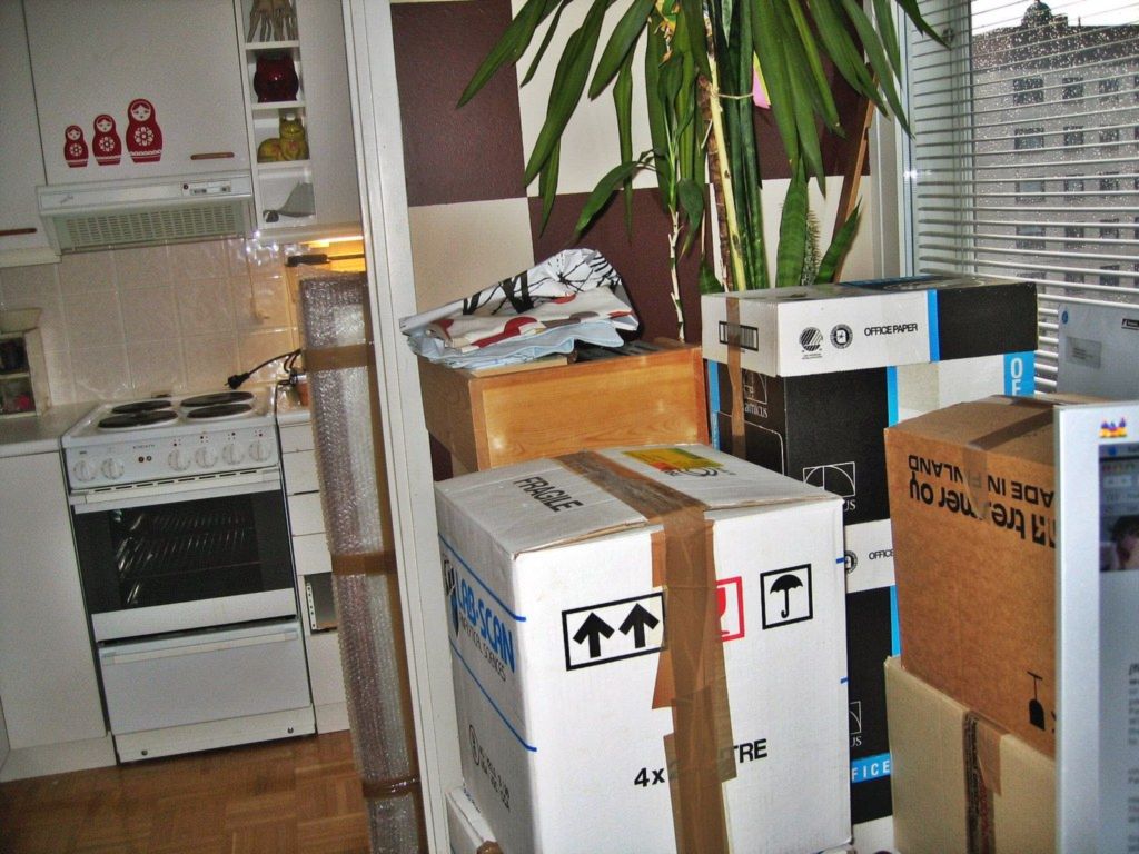 Packed moving boxes stacked in a small apartment kitchen beside a white stove